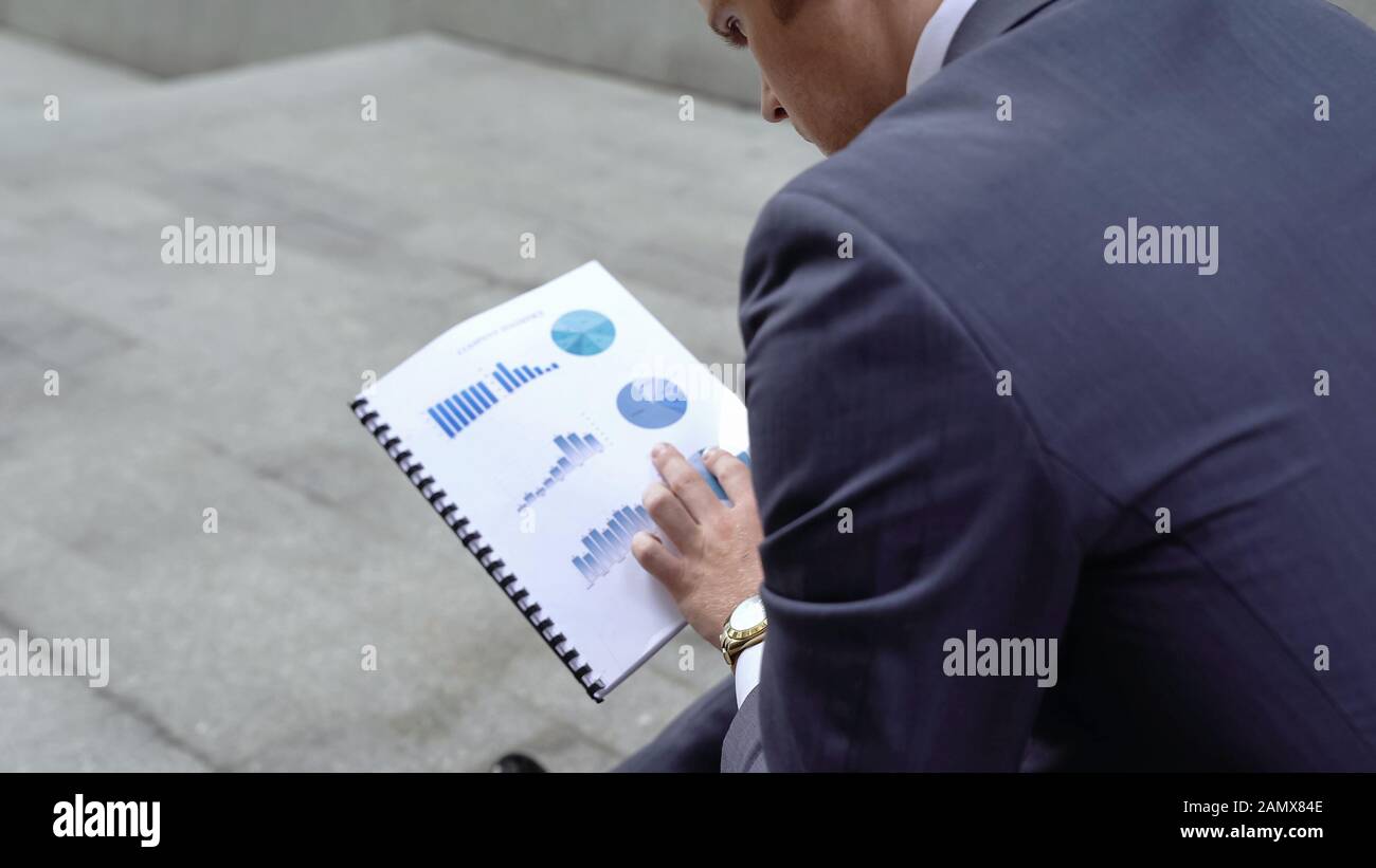 Pensive financial consultant examining business graphs, company going bankrupt Stock Photo