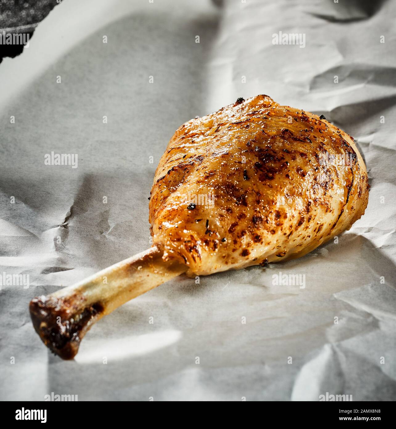 Grilled seasoned spicy chicken leg or drumstick on crumpled white paper