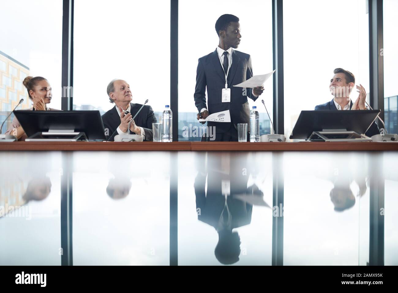 African young businessman standing and performing with financial report and people clapping to him at conference Stock Photo