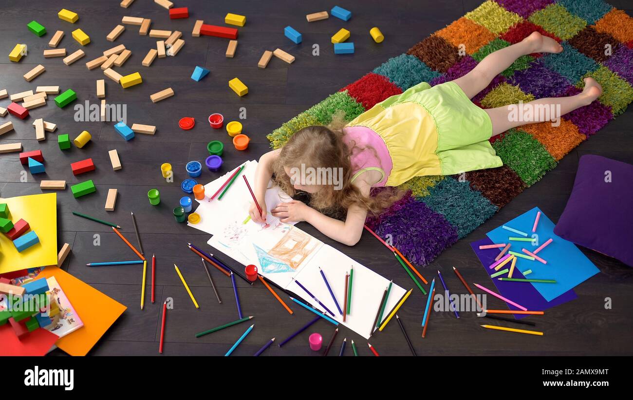 Cute little girl lying on floor and drawing with color pencils on paper ...