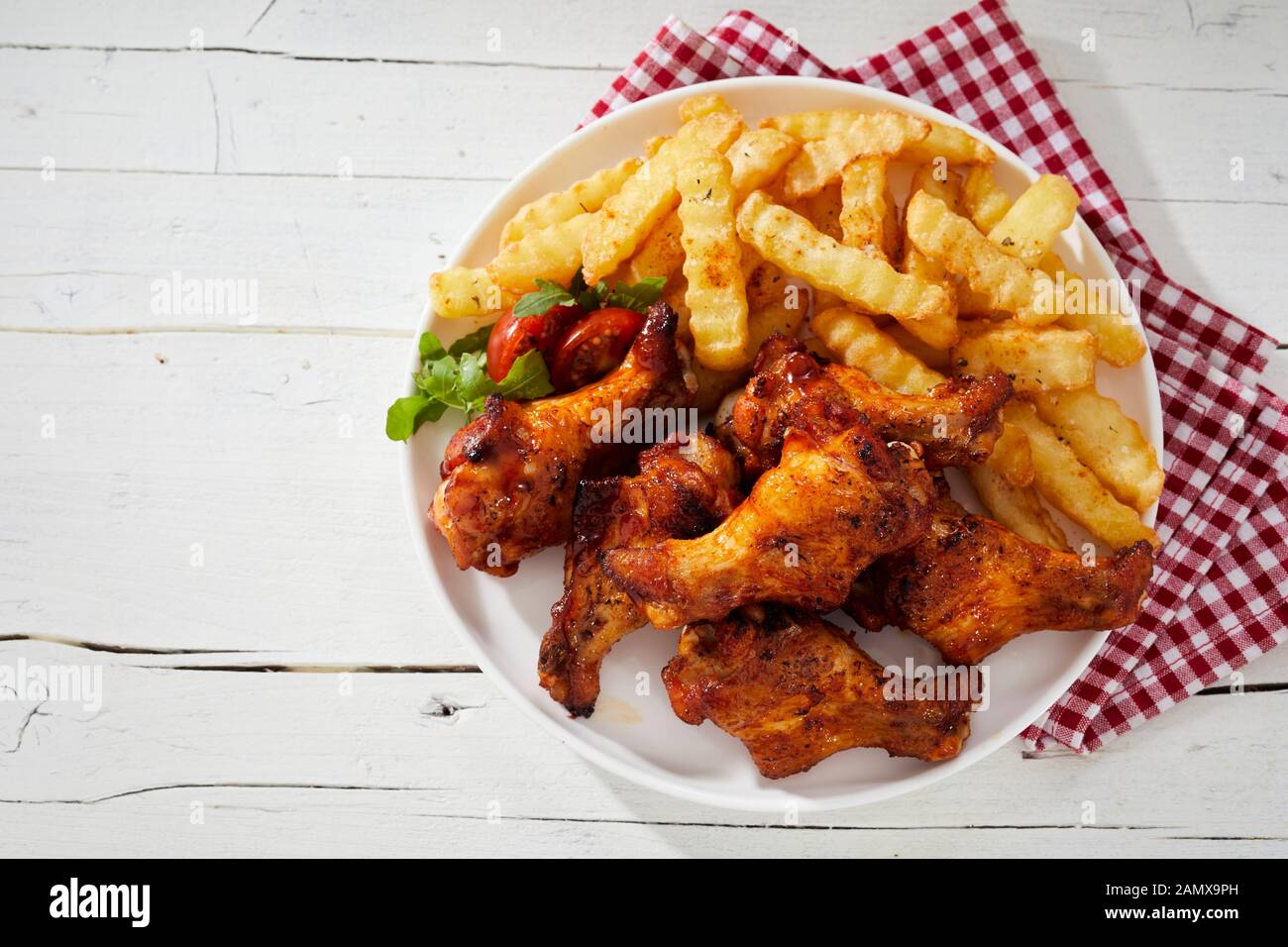 Crispy barbecued spicy chicken wings with oven baked crinkle cut potato chips and salad trimming on a plate viewed from overhead Stock Photo