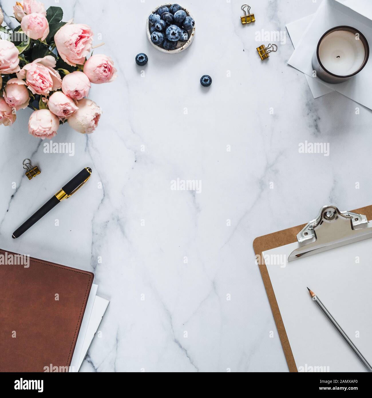 Top view of female home office with copy space in center. Clipboard, flowers, scented candle on white marble. Feminine home office mock up with copy space for text or design. Flat lay Stock Photo