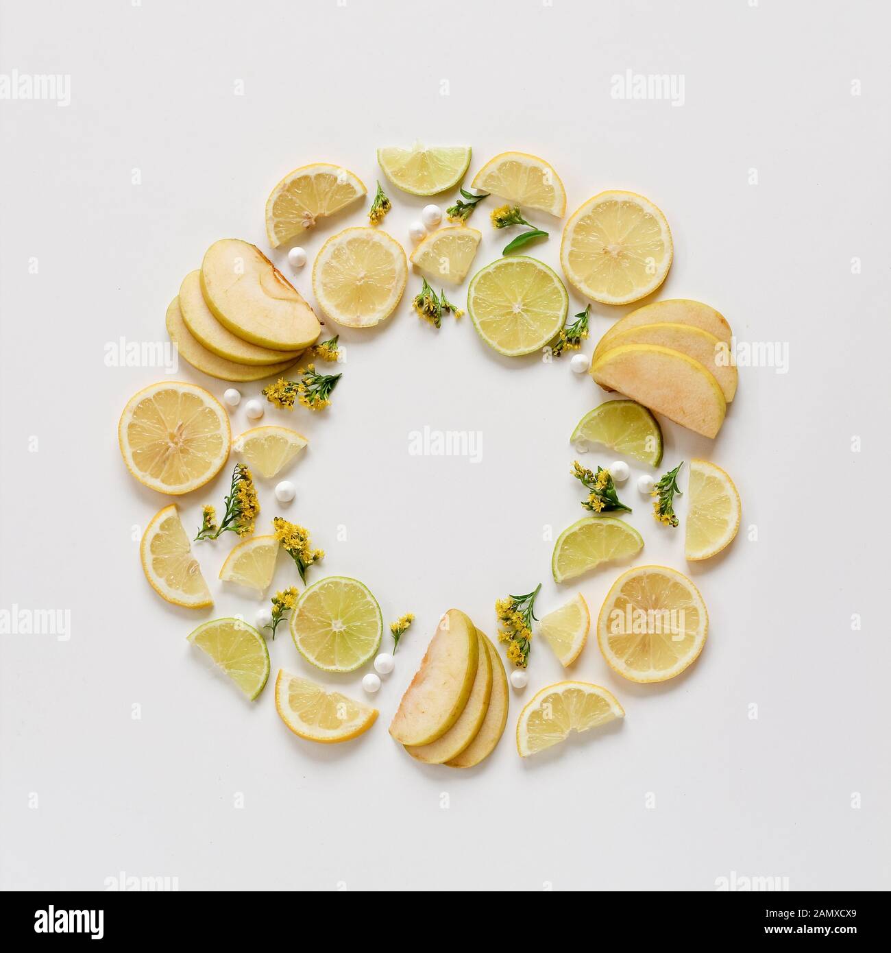 Creative pattern of sliced fruits and yellow blooms. Green apple, green and yellow lemons arranged in a circle. Flat lay with copy space Stock Photo