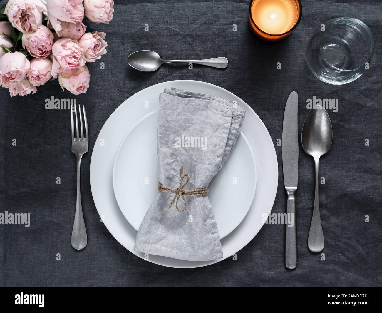 Beautiful table setting with pink spray roses and candle on gray linen tablecloth. Festive table setting for wedding dinner with gray linen napkin on plate. Holiday dinner at home, with white plates Stock Photo