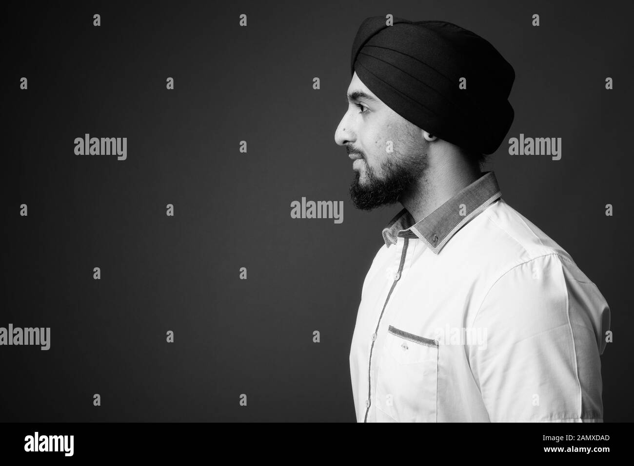Young bearded Indian Sikh man wearing turban against gray background Stock Photo
