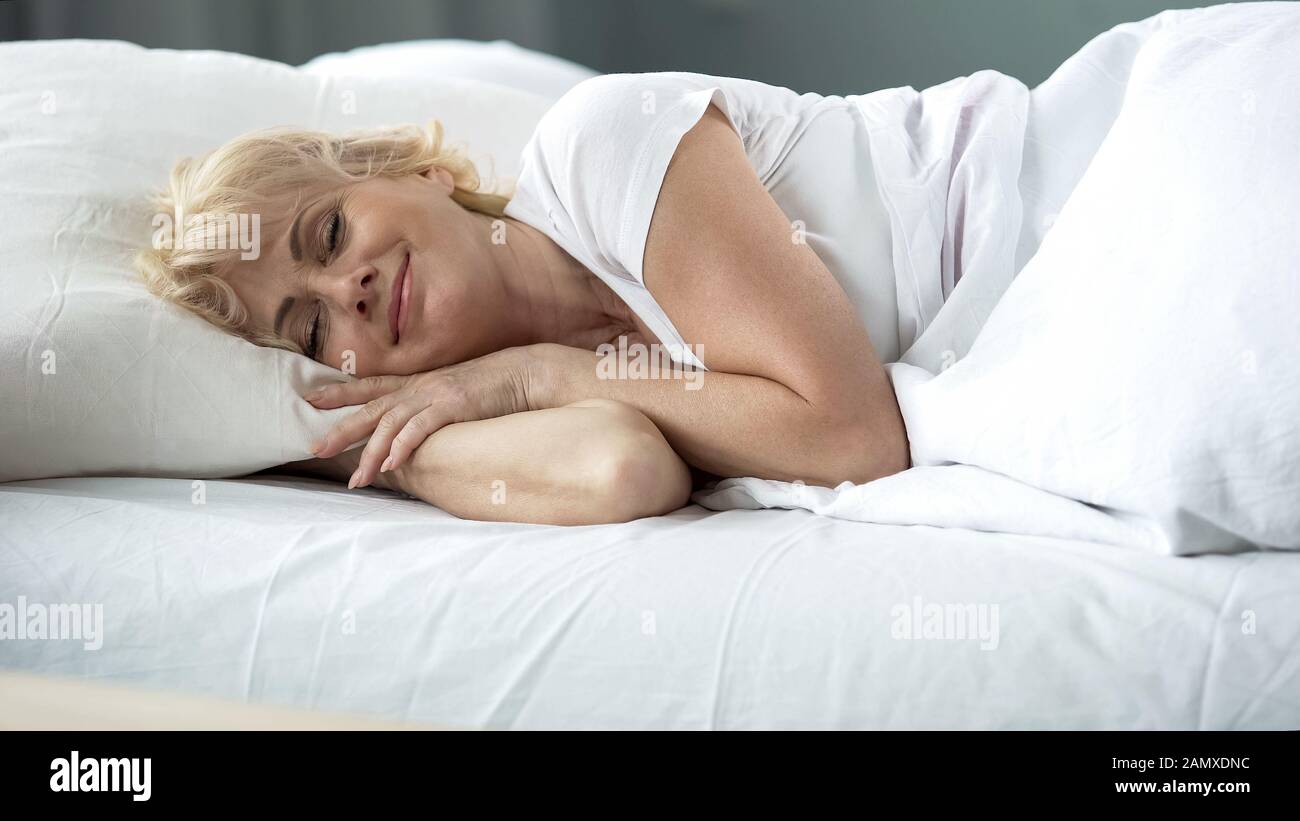 Happy middle-aged female sleeping in bed on orthopedic mattress, healthy rest Stock Photo