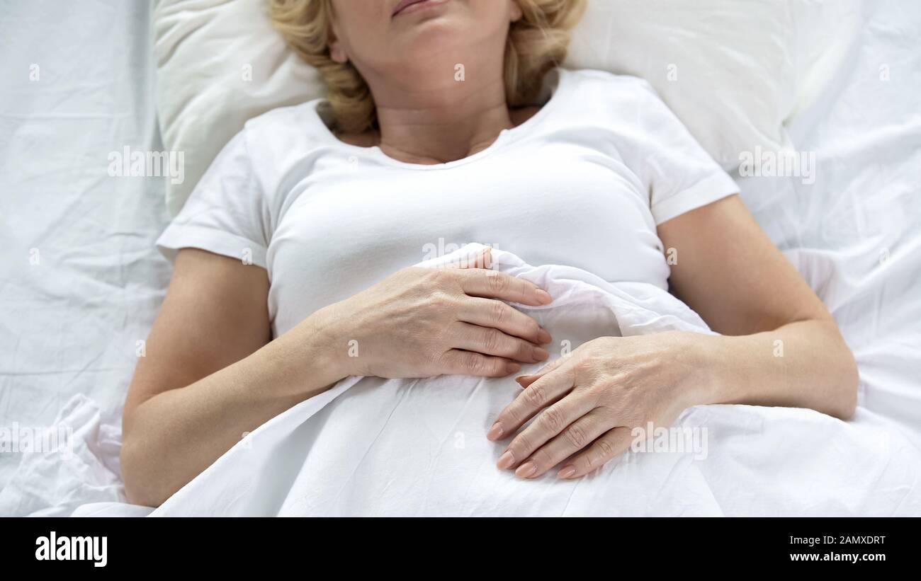 Senior woman sleeping in her bed, top view wrinkled hands, retirement