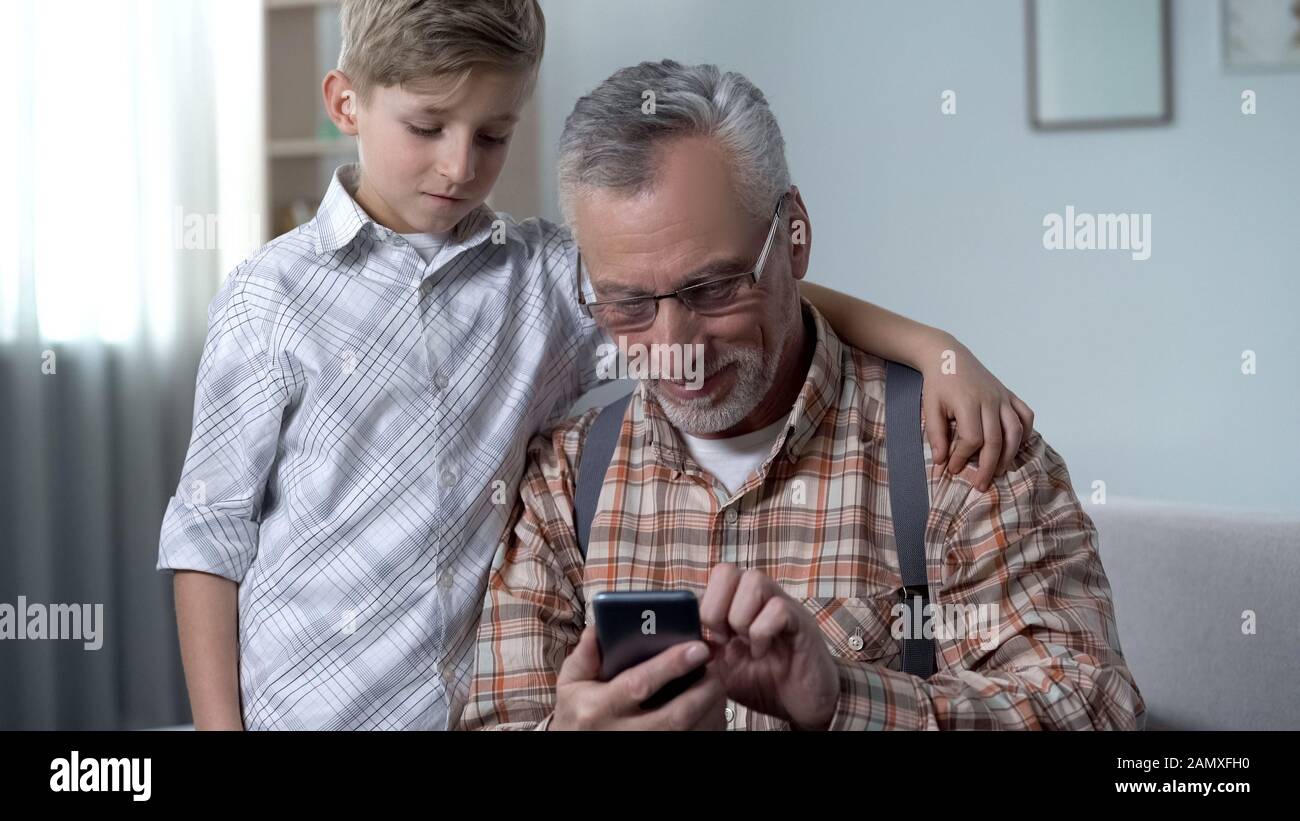 Boy helping grandfather to better understand smartphone, digital generation gap Stock Photo