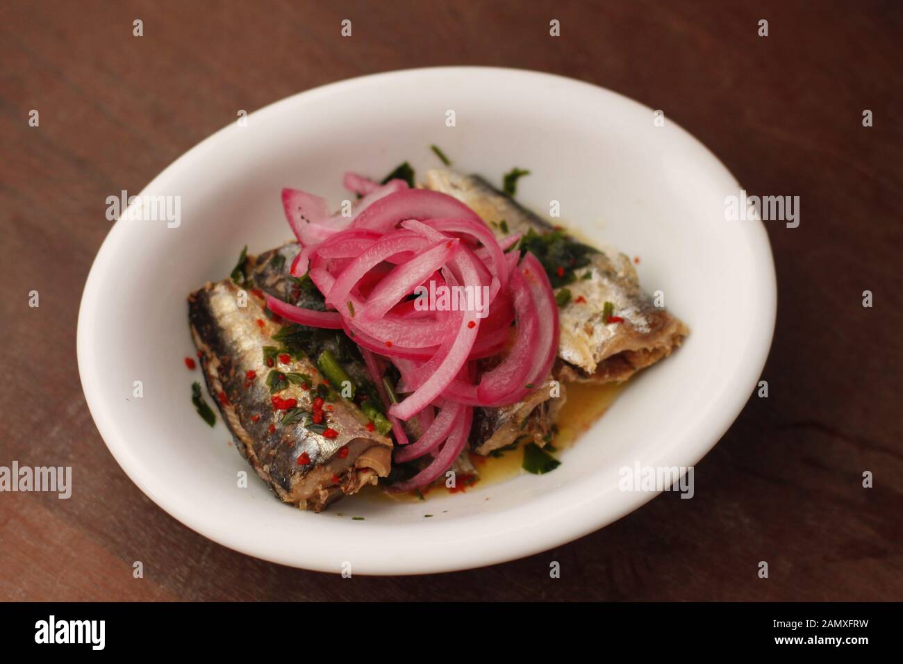 Sardines escabeche with fresh herbs covered with marinated red onions in white oval plate Stock Photo