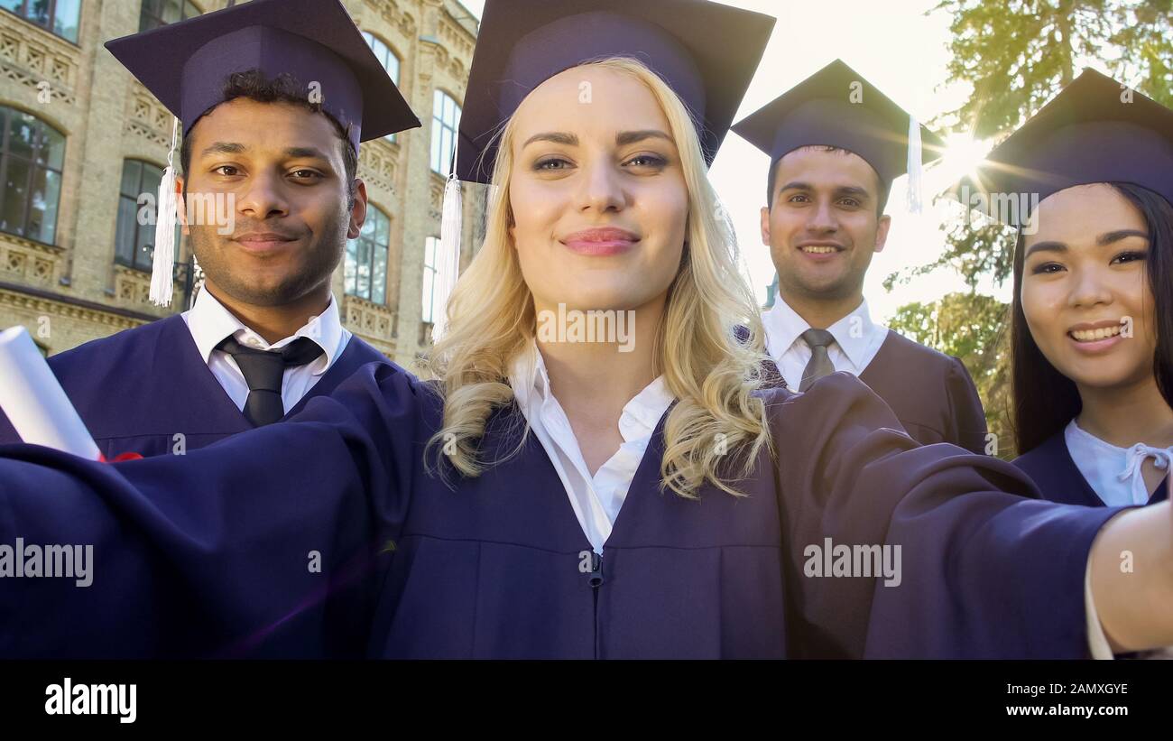 Students in academic regalia taking selfie on graduation day, achievement Stock Photo