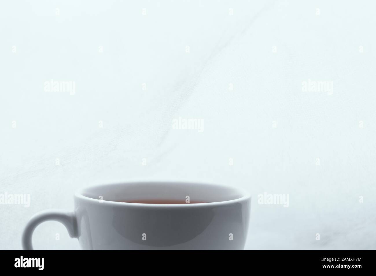 Cropped simple white cup filled with tea on the left on white ...