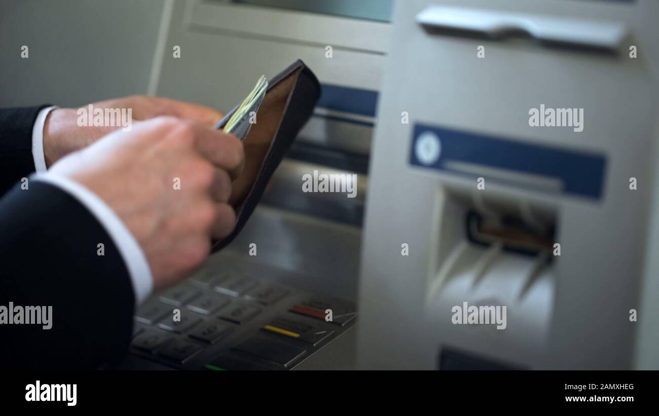 Mans hands putting dollars in wallet, cash withdrawn from ATM, travelling abroad Stock Photo