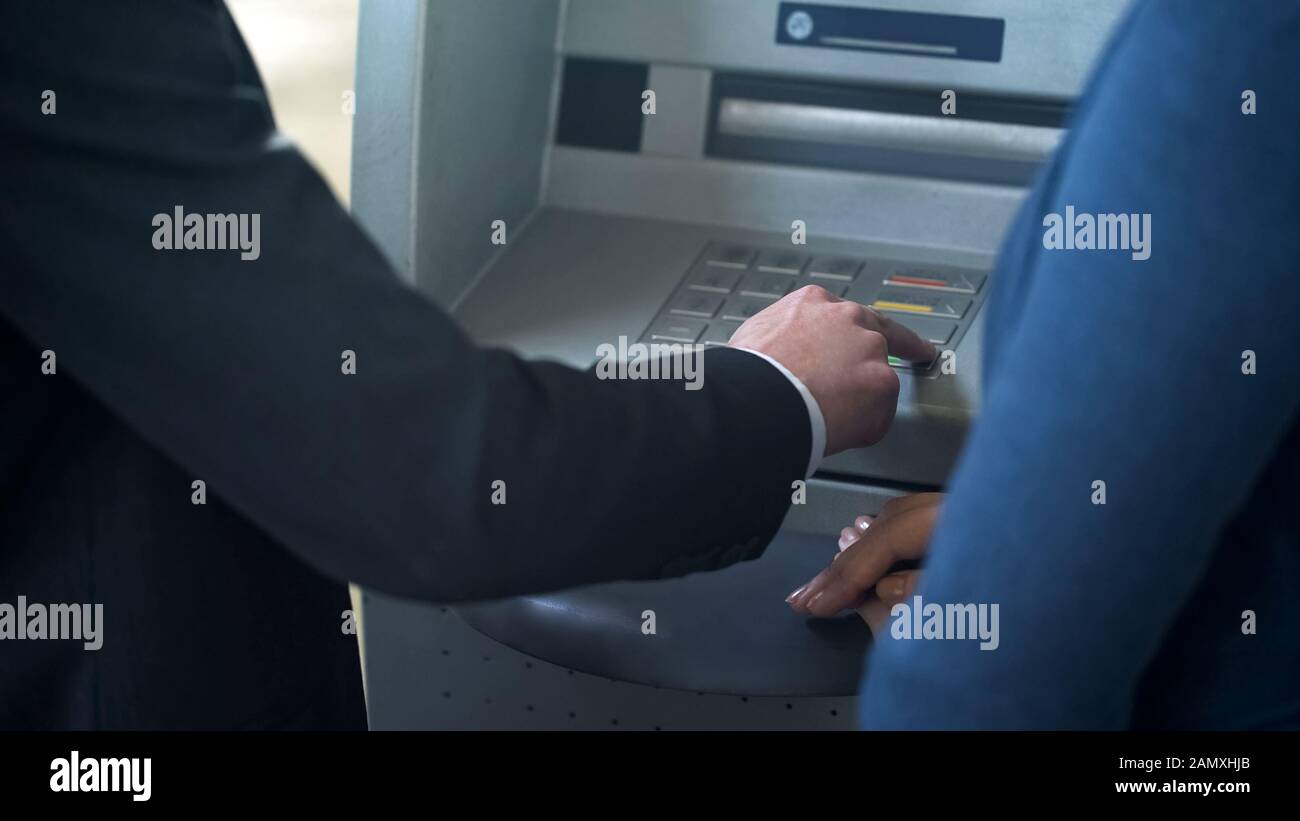 Female bank employee showing new client how to work with ATM, good ...