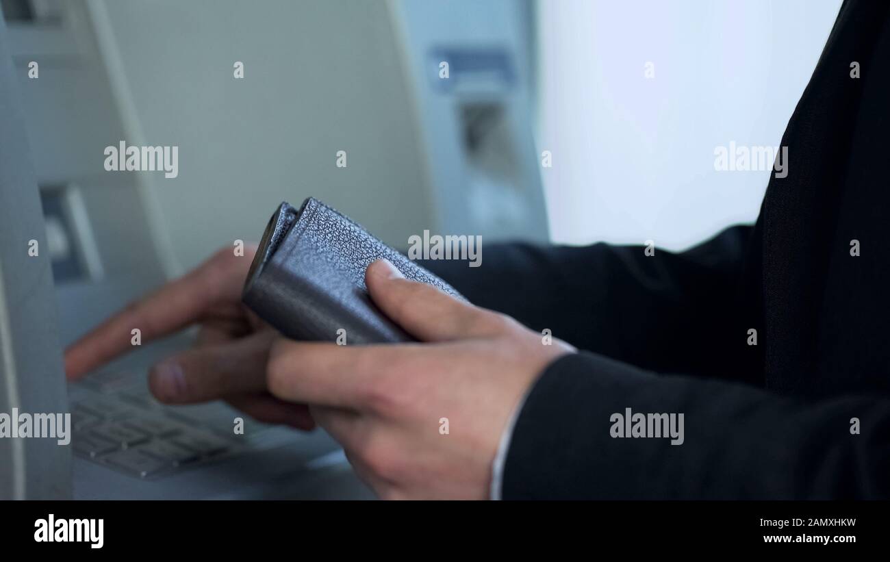 Man with purse inserting card in ATM to withdraw cash and receive balance report Stock Photo