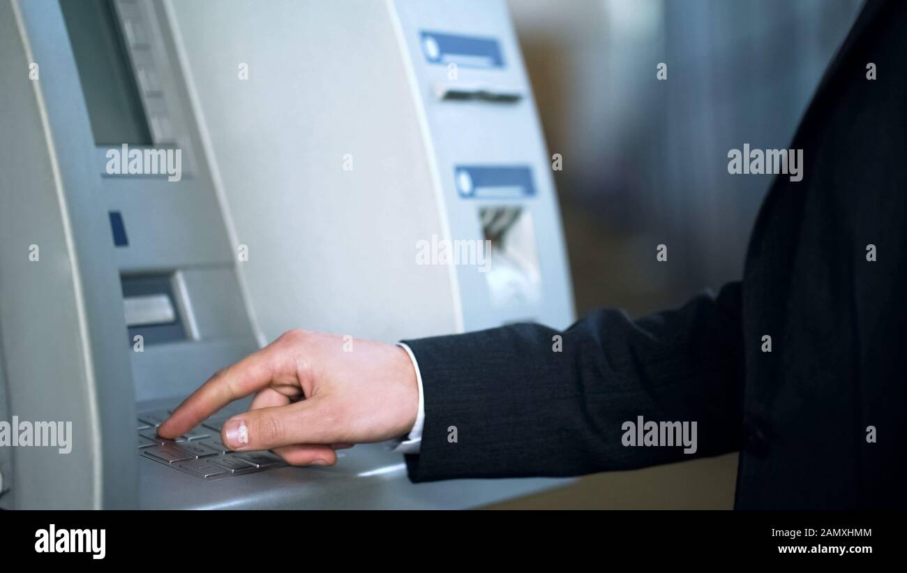 Businessman entering pin code to receive money, banking for travelers, trip Stock Photo