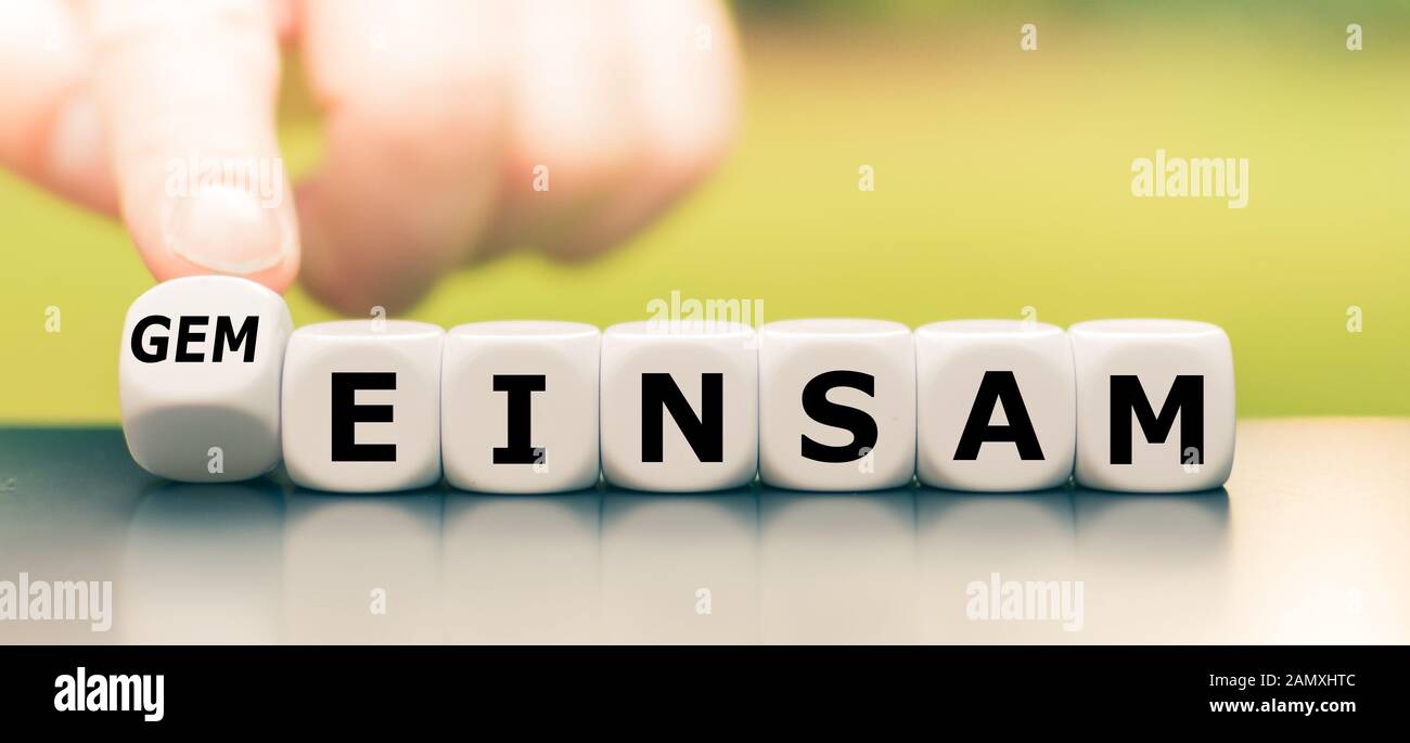 Hand turns a dice and changes the German word "einsam" ("lonely" in English) to "gemeinsam" ("together" in English). Stock Photo