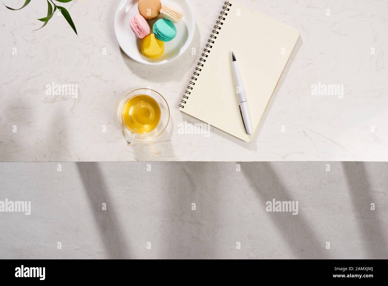 Top view of notebook, pen, cake macaron and tea mug on white background. Flatlay. Stock Photo