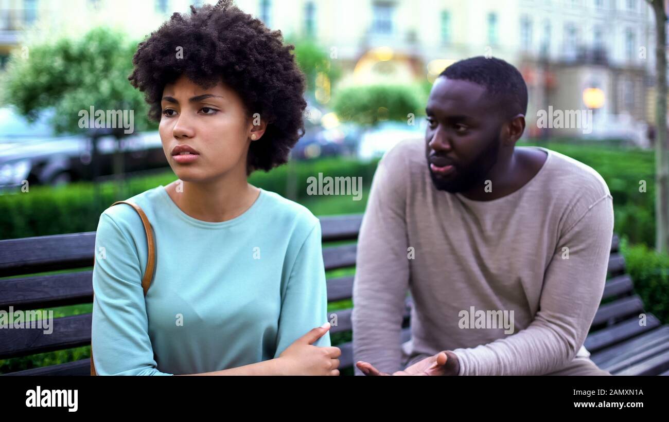Young man talking to offended girlfriend on bench, jealous woman, break up Stock Photo