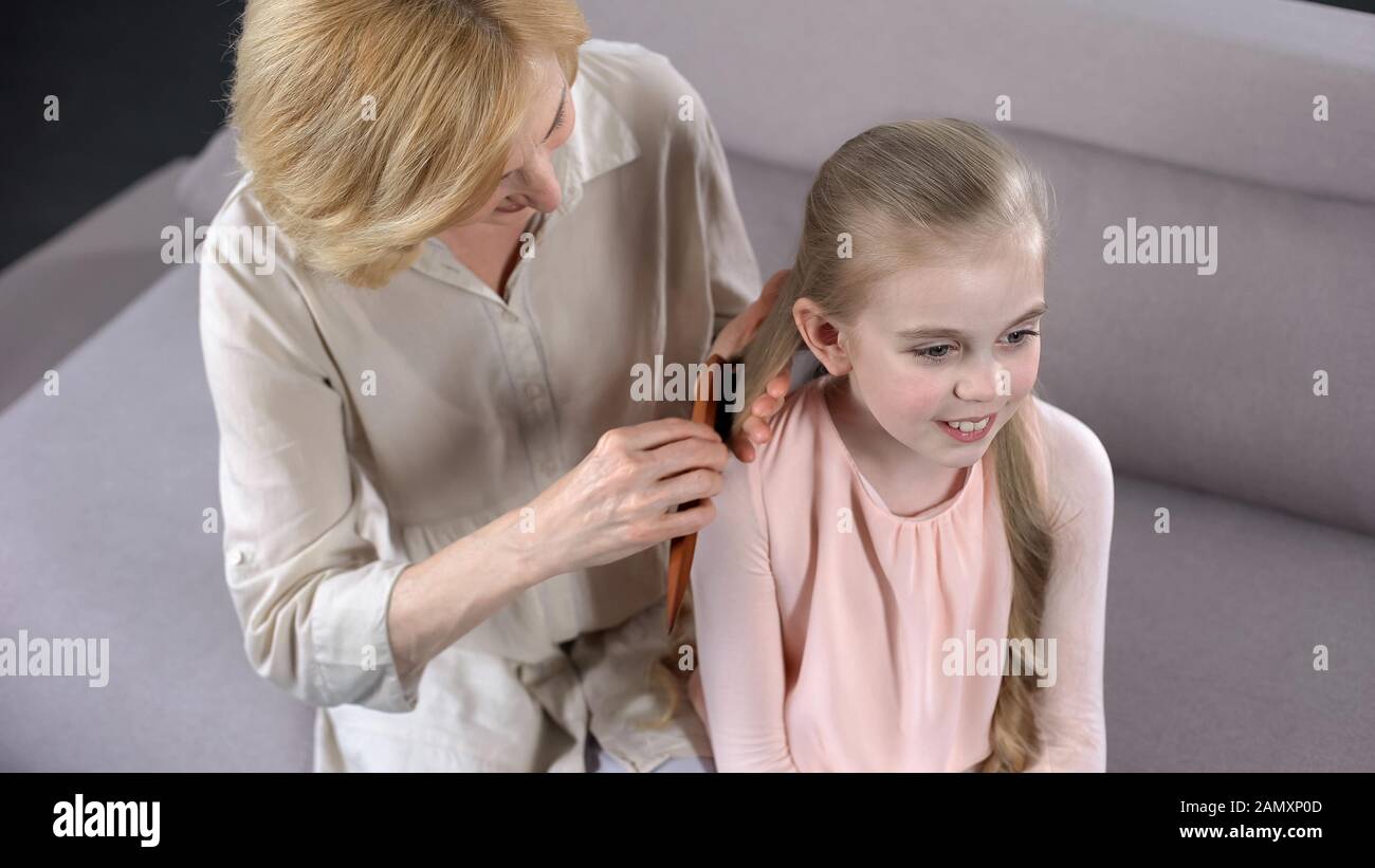 Caring mature mother combing daughters blond hair, beauty time, relationship Stock Photo