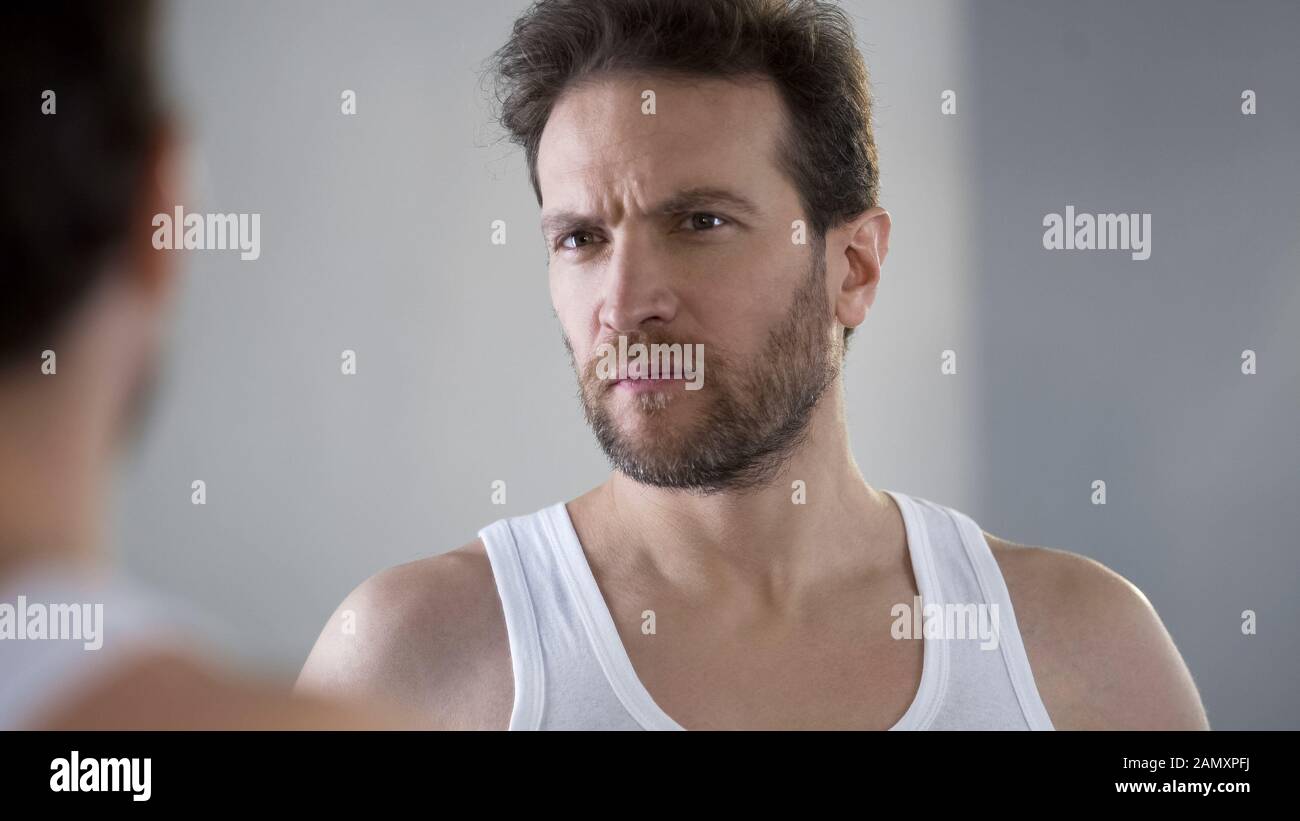 Middle aged man looking at mirror reflection, dissatisfied with skin condition Stock Photo