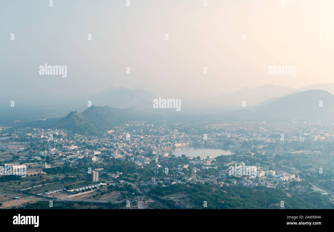 Elevated and wide view of Pushkar town with holy lake and buildings flanked by Aravalli Hill at sunrise in summer. Rajasthan, India. Stock Photo