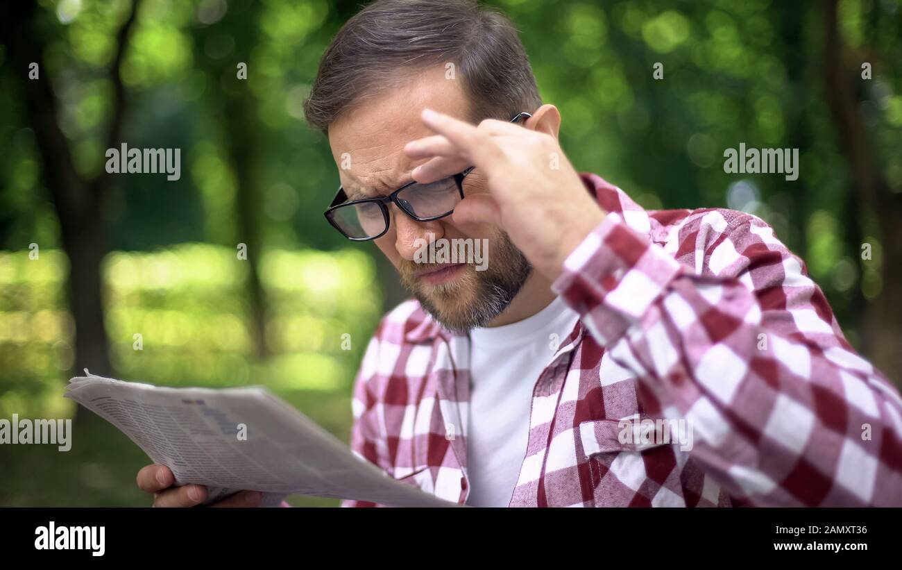 Aging man in eyeglasses trying to read newspaper in park, farsightedness, myopia Stock Photo