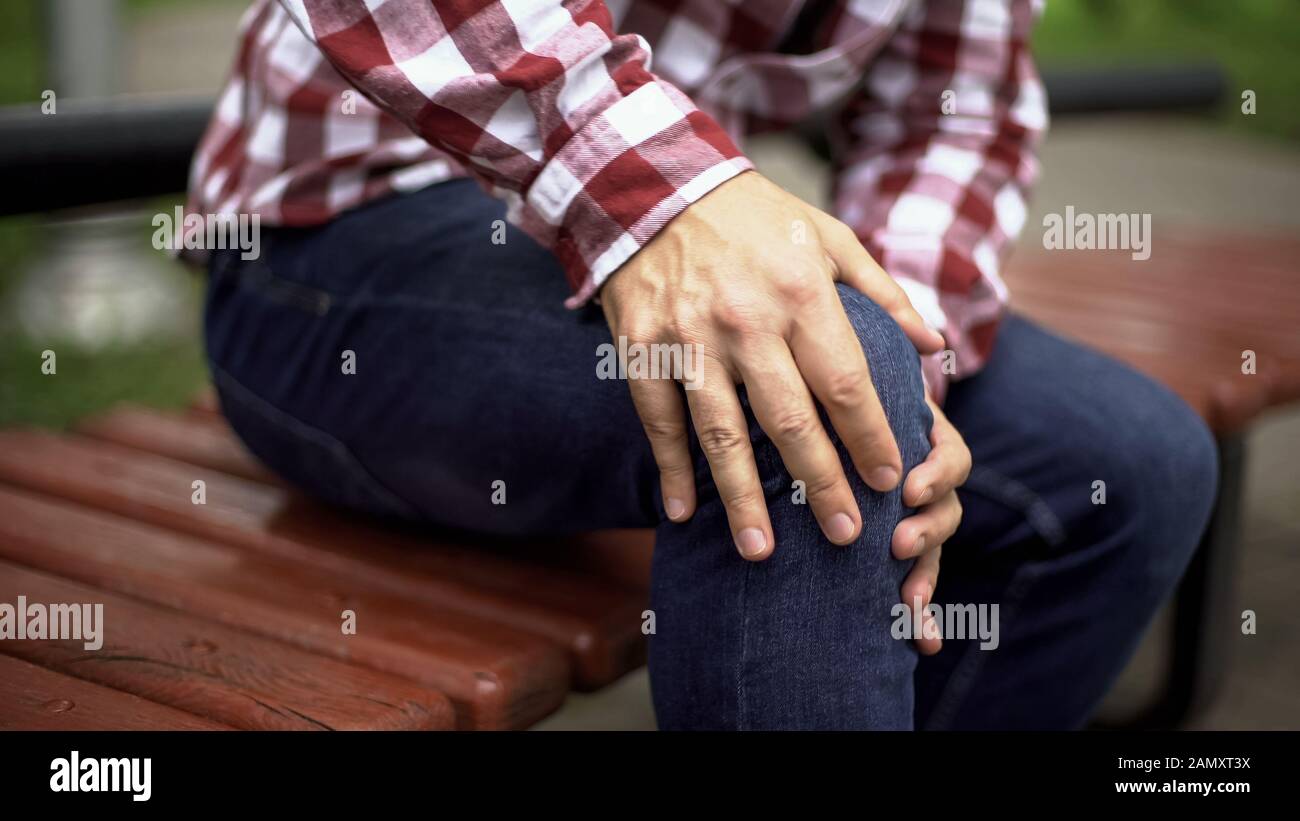 Man sitting on bench feeling sharp knee pain, osteoarthritis, injury