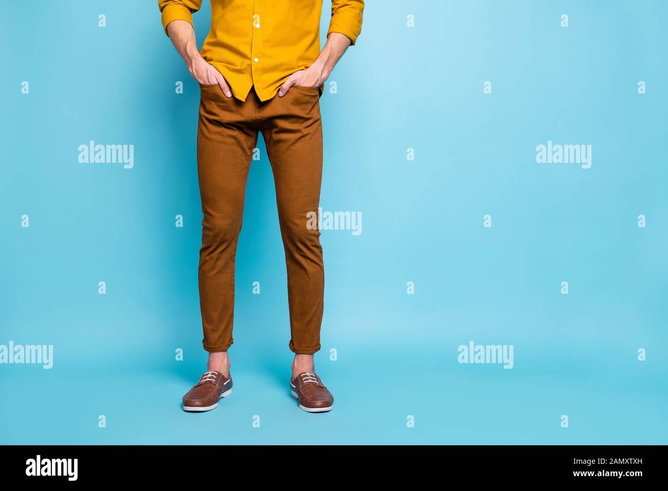 Cropped view of his he young guy wearing brown pants orange formal casual shirt holding hands in pockets isolated on bright vivid shine vibrant blue Stock Photo