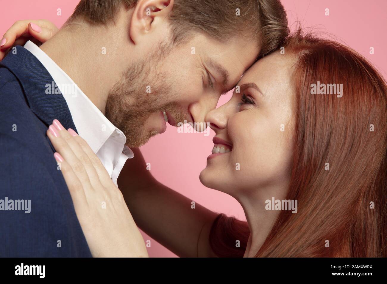 Valentine's day celebration, close up of caucasian couple's kissing and smiling on coral studio background. Concept of human emotions, facial expression, love, relations, romantic holidays. Stock Photo