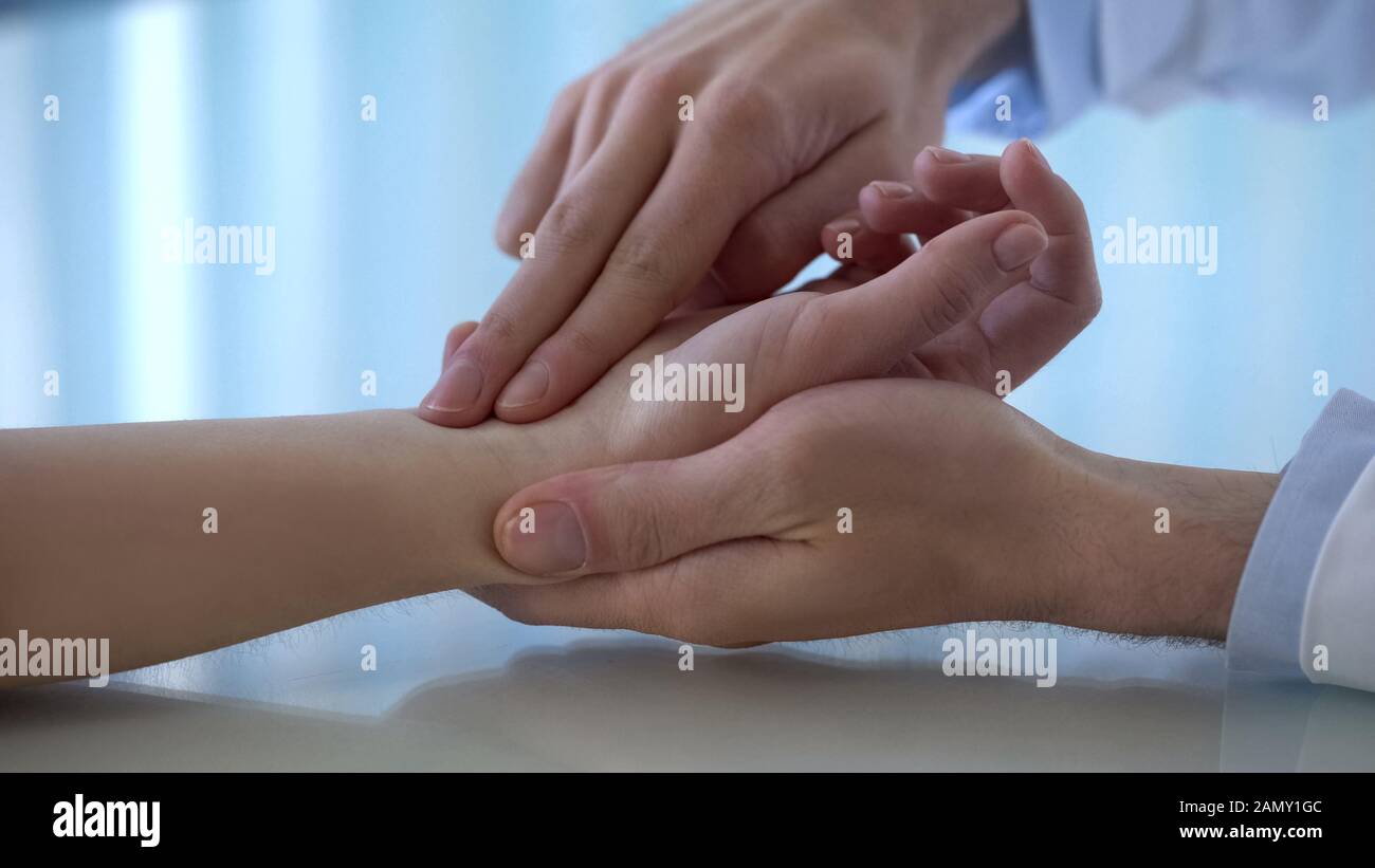 Family doctor measuring pulse of female patient at hospital, medicine and health Stock Photo