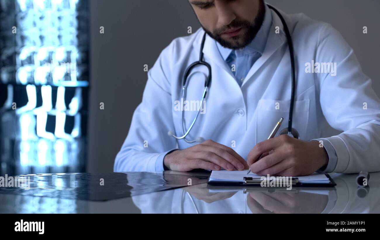 Experienced doctor examining x-ray and writing diagnosis in medical form, health Stock Photo