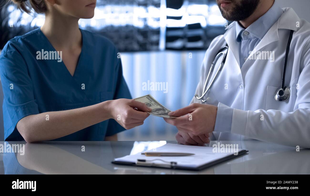 Young female intern giving bribe to head physician, dishonest people, corruption Stock Photo