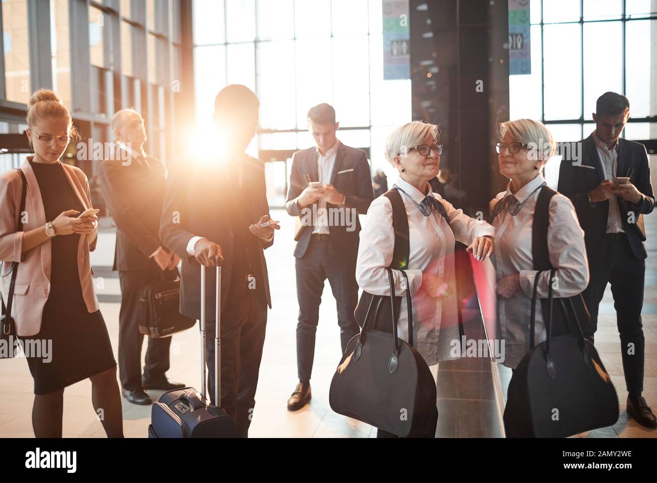 Group of people with luggage using their gadgets while standing in a queue at the airport Stock Photo
