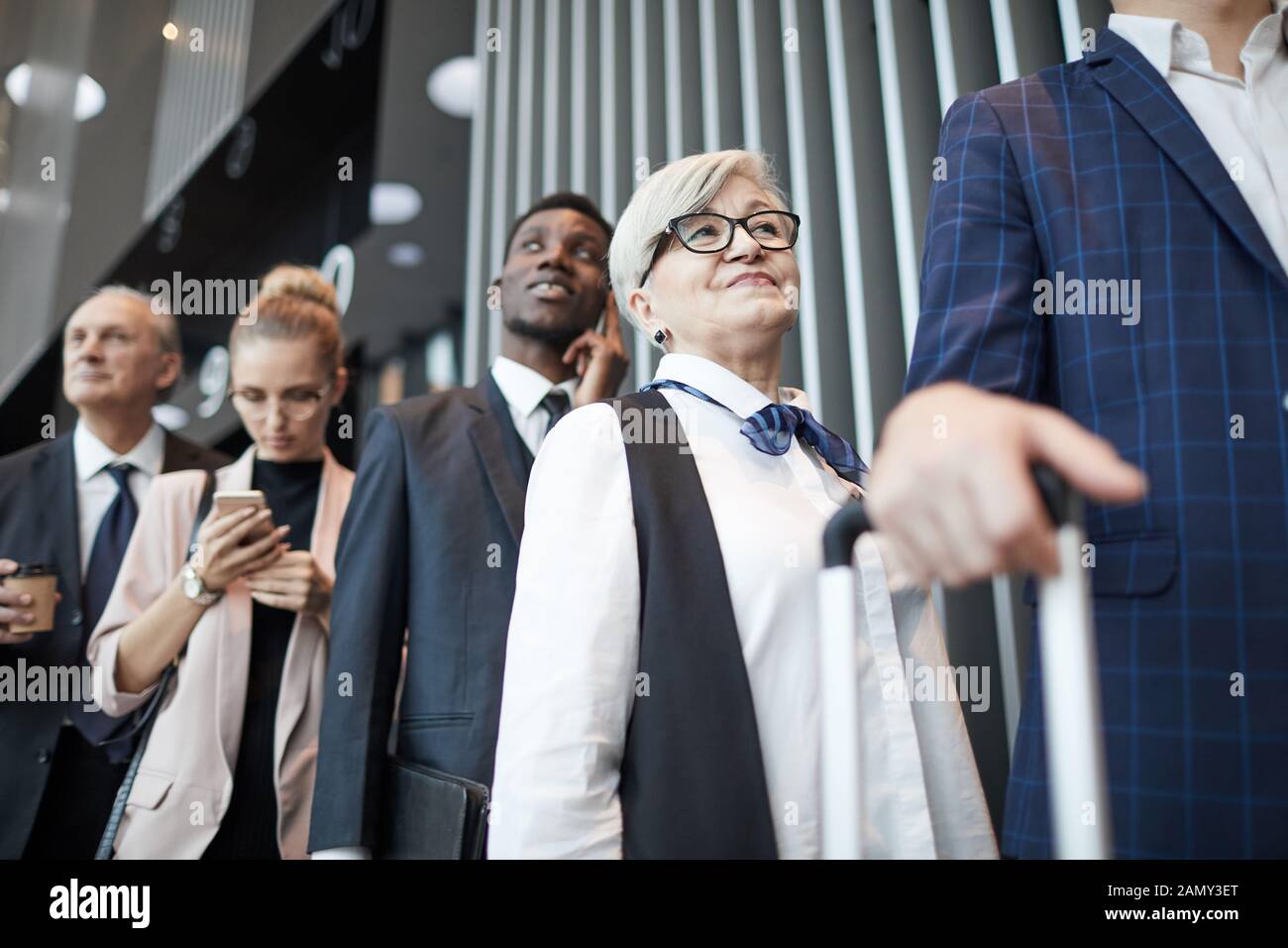 Senior woman in eyeglasses standing in the queue with other people she registering before flight at the airport Stock Photo