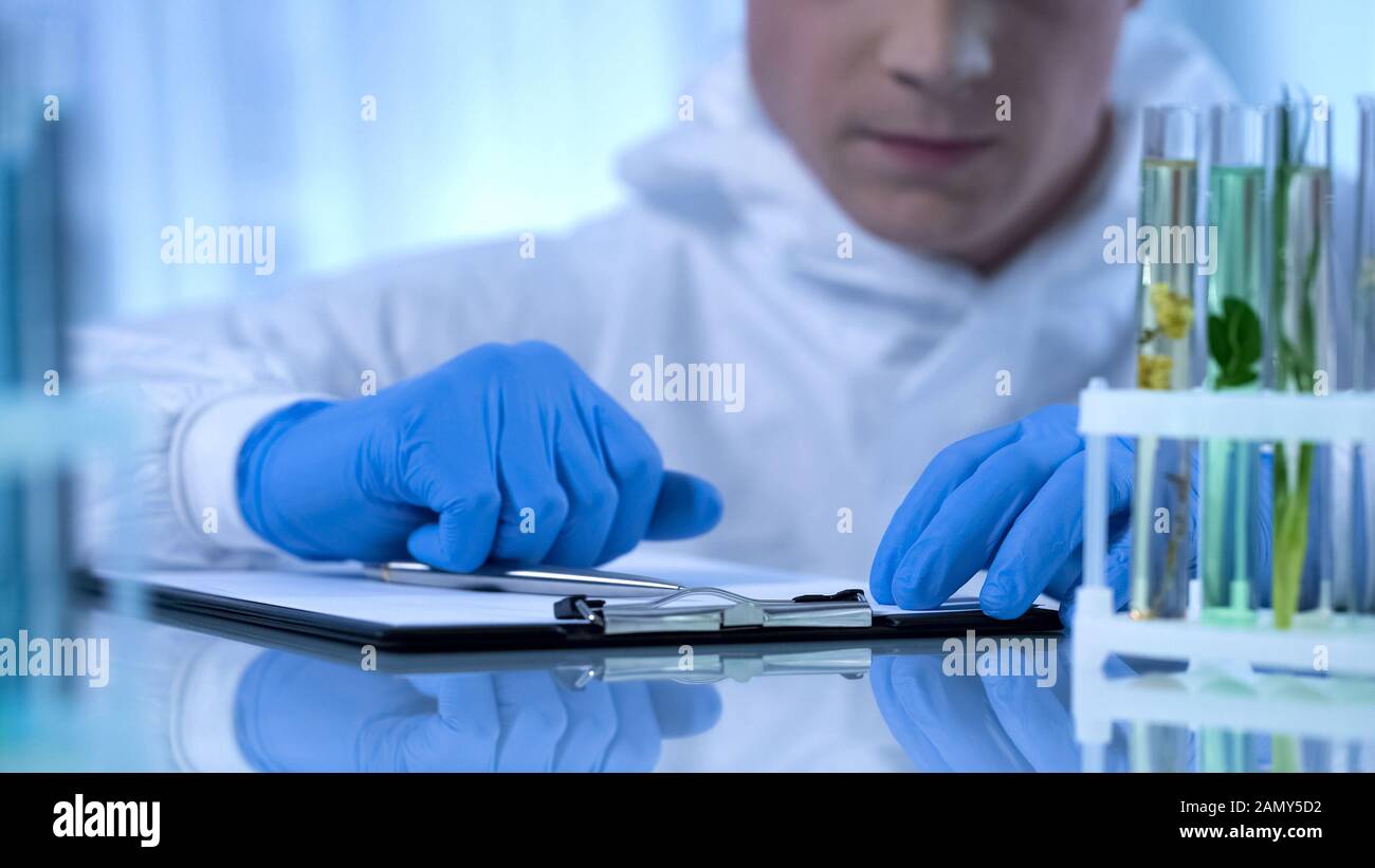 Biologist observing plant in test tube, writing information about growth changes Stock Photo