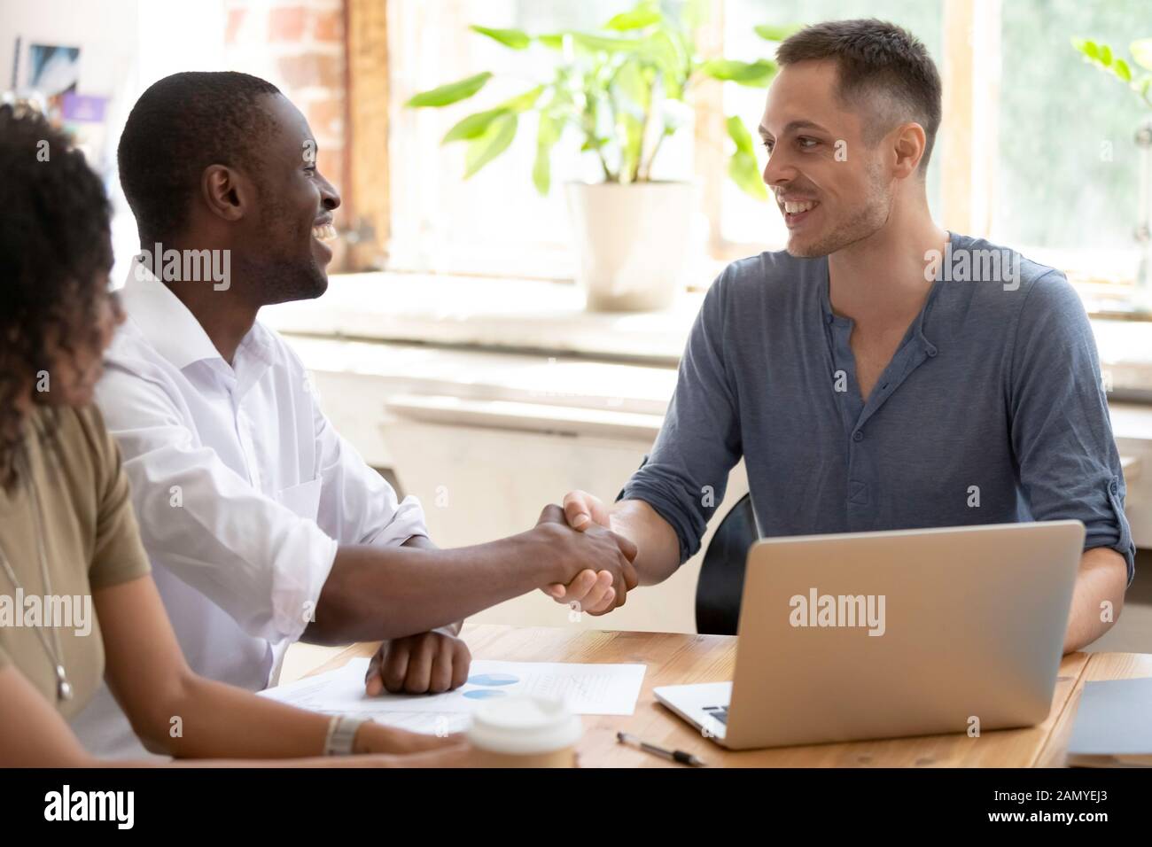 Smiling multiracial male colleagues handshake greeting at meeting Stock Photo