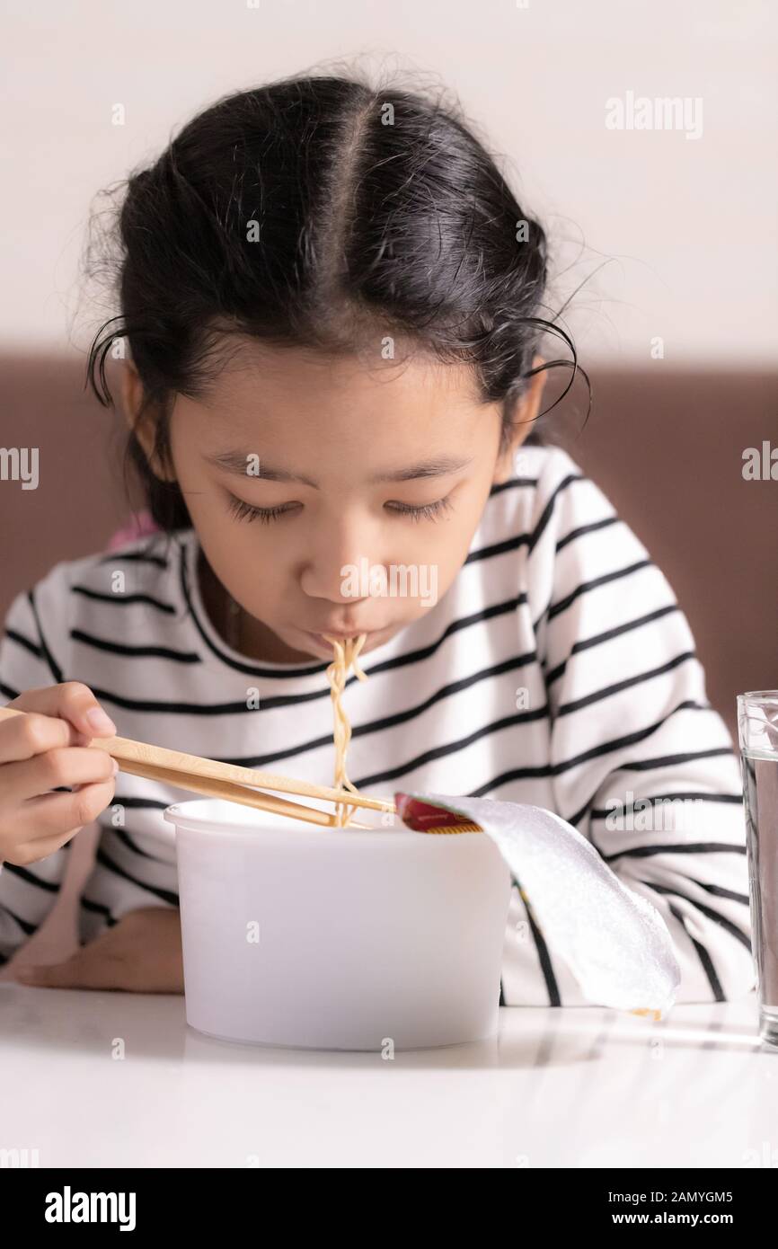 Little Asian girl sitting at white table to eating instant noodle select focus shallow depth of filed Stock Photo