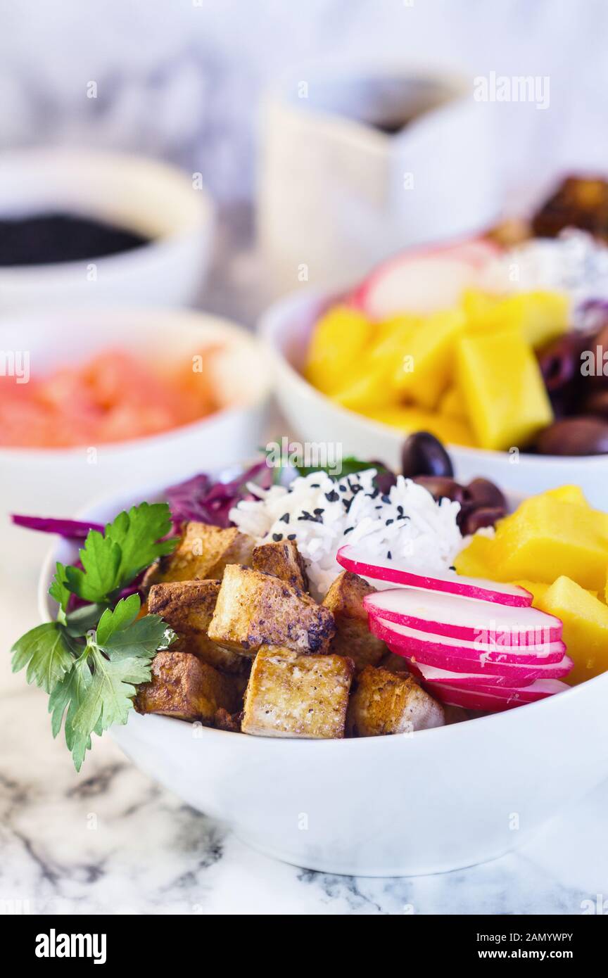 Healthy vegan poke bowl or Buddha bowl with basmati rice, mango, fried tofu, purple cabbage, radishes, kalamata olives, pickled ginger and black sesam Stock Photo