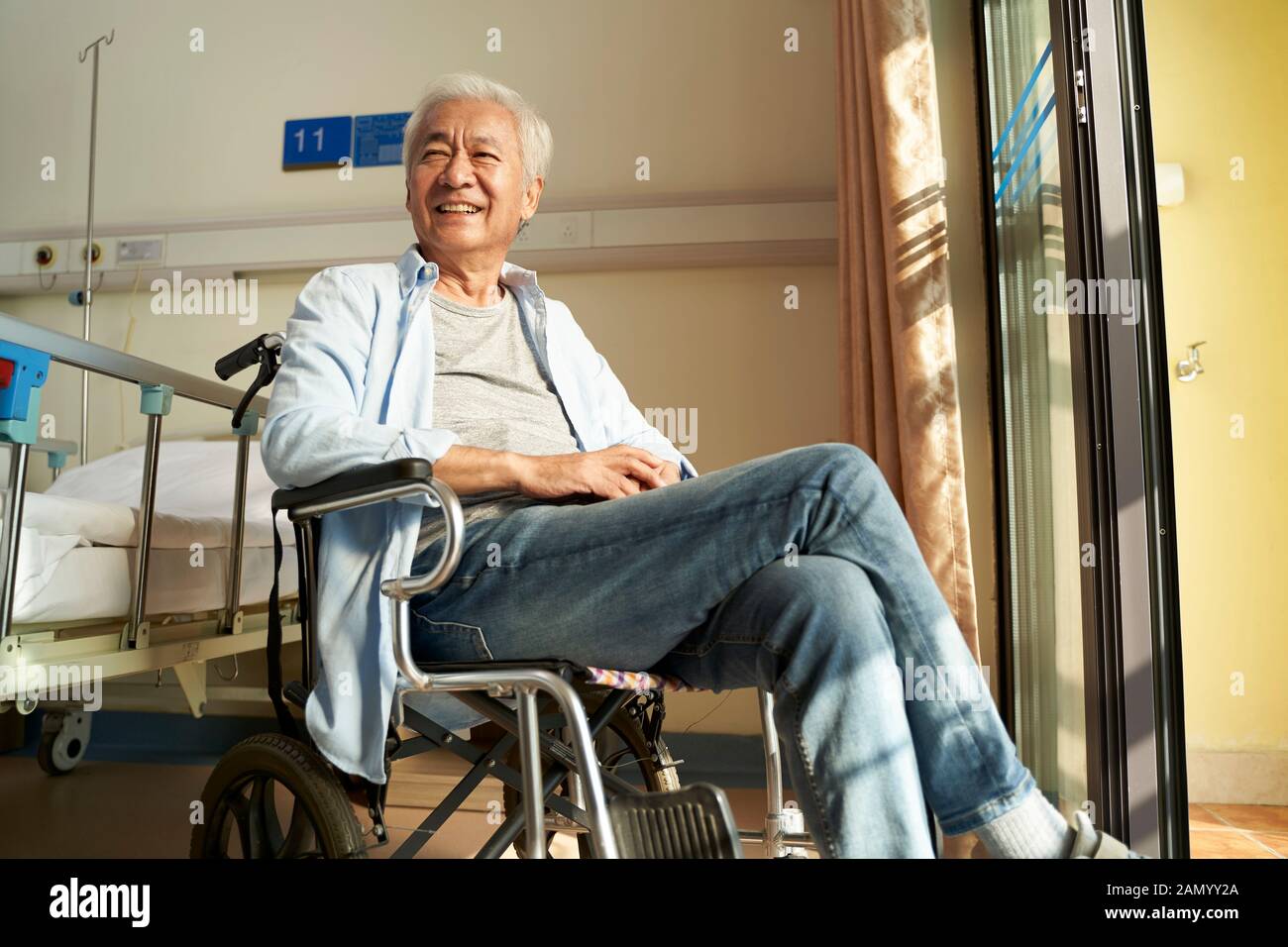 asian old man sitting in wheel chair in nursing home or hospital ward looking happy and content Stock Photo