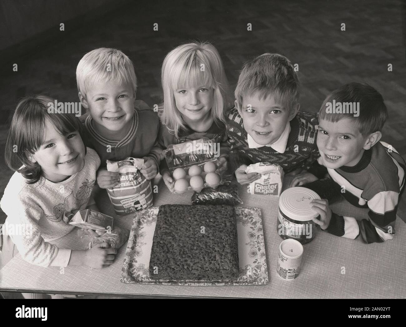 1980s, historical, happy young nursery children with the ingredients for a cake that they have just baked, including flour, eggs, and caster sugar, England, UK. Stock Photo