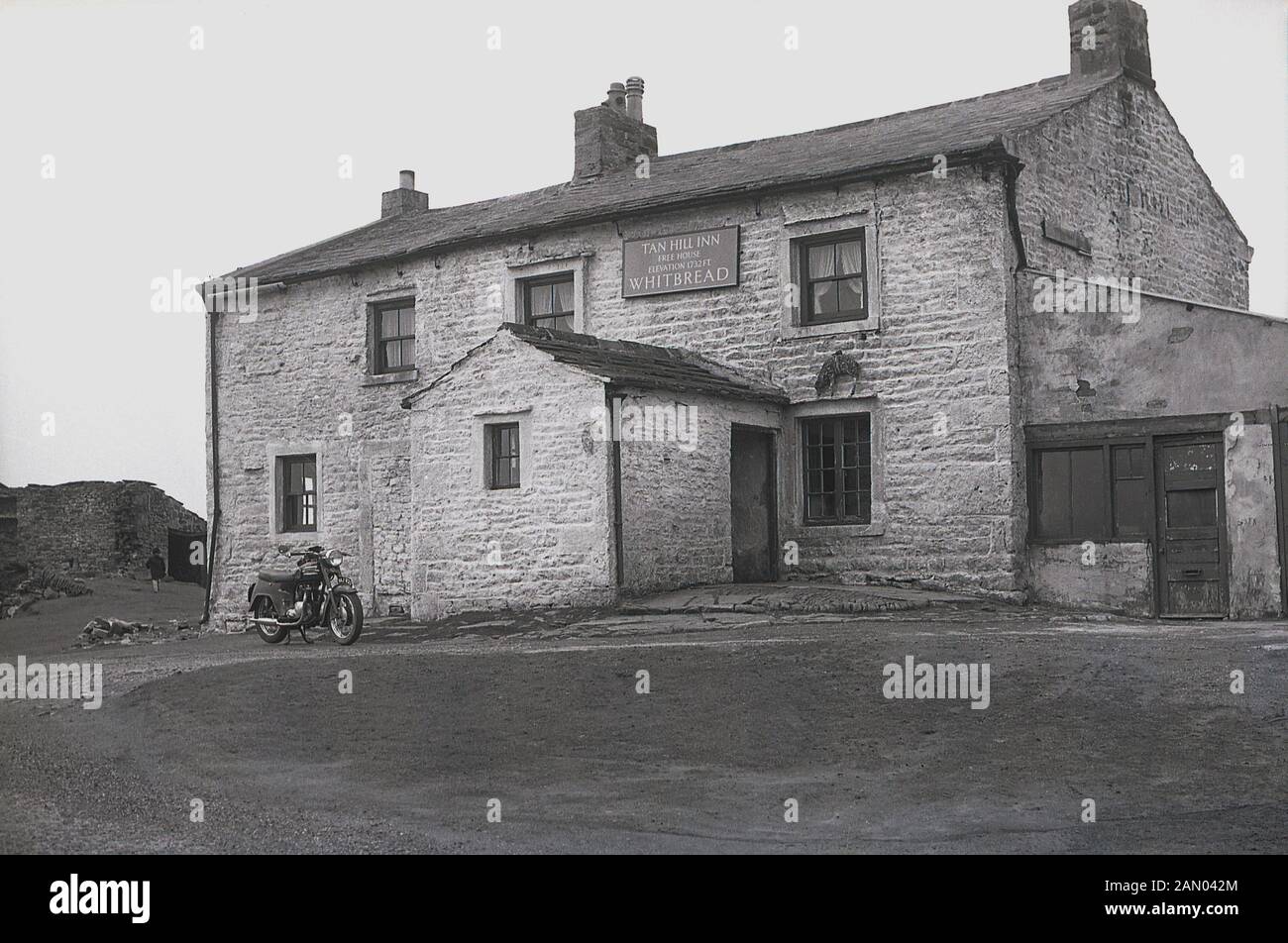 1965, historical picture from this era, a motorbike parked outside the Tan Hill Inn, a unique and historic 17th Century pub standing high-up in the Yorkshire Dales, England, UK. At a height of 1732 ft above sea level, it is the highest pub in Great Britain and stands directly on the Pennine Way, Britain's first long-distance footpath which Alfred Wainwright started and which opened in 1965. Stock Photo