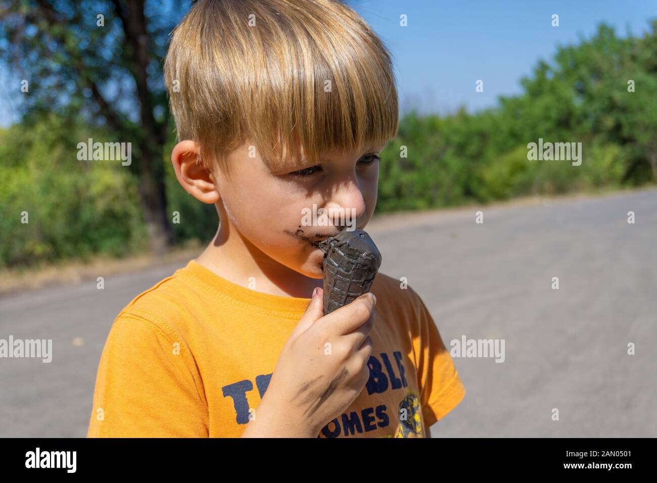 Black ice cream in the hands of a child, the boy eats black ice cream, dirty face and mouth. Stock Photo