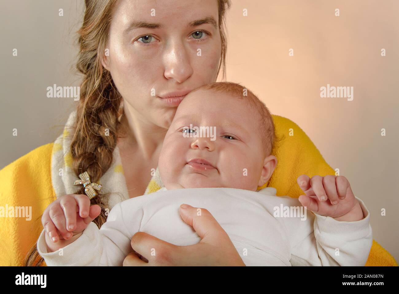 Mom holds the baby in her arms and poses for the camera in the studio, the concept of love and unity and care for loved ones and younger ones. Stock Photo