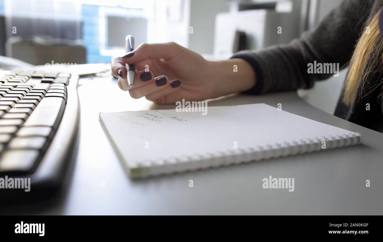 Female hand holding pen, taking notes in her notebook, searching for data on PC Stock Photo