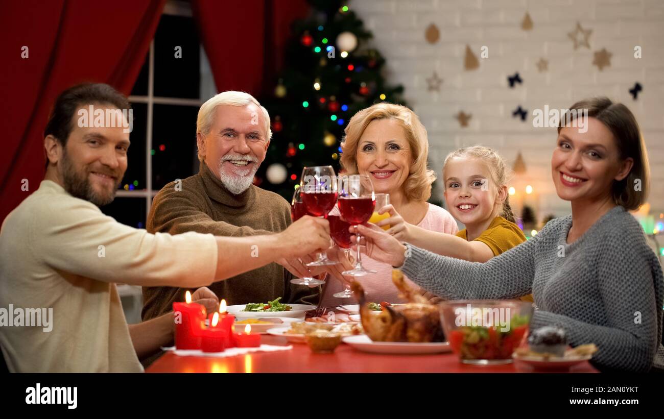 Big friendly family clinking glasses with wine on Xmas eve, looking into camera Stock Photo