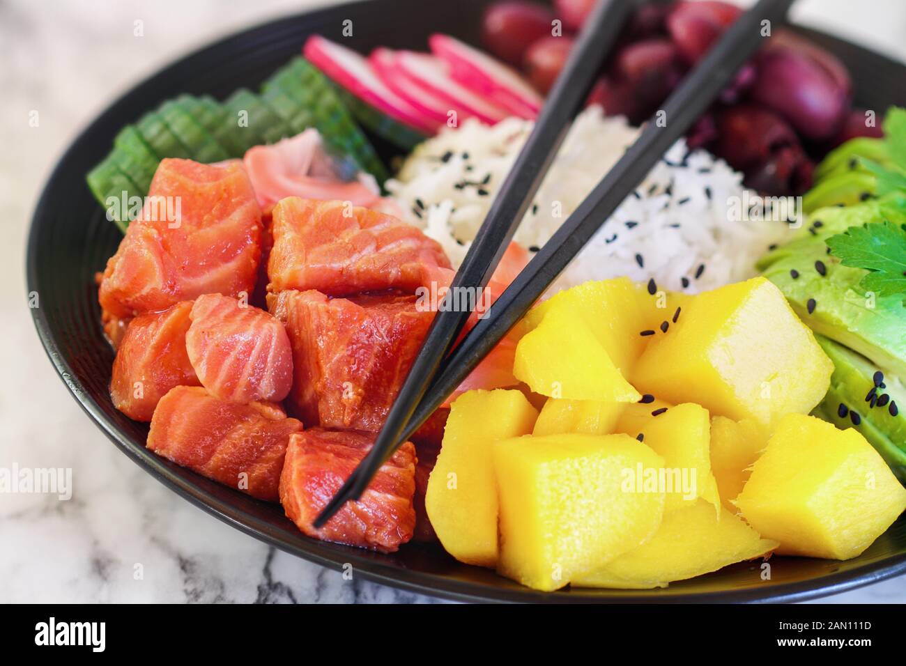 Hawaiian poke bowl with basmati rice, mango, raw salmon, avocado. radishes, cucumber, kalamata olives, pickled ginger and black sesame seeds. Selectiv Stock Photo