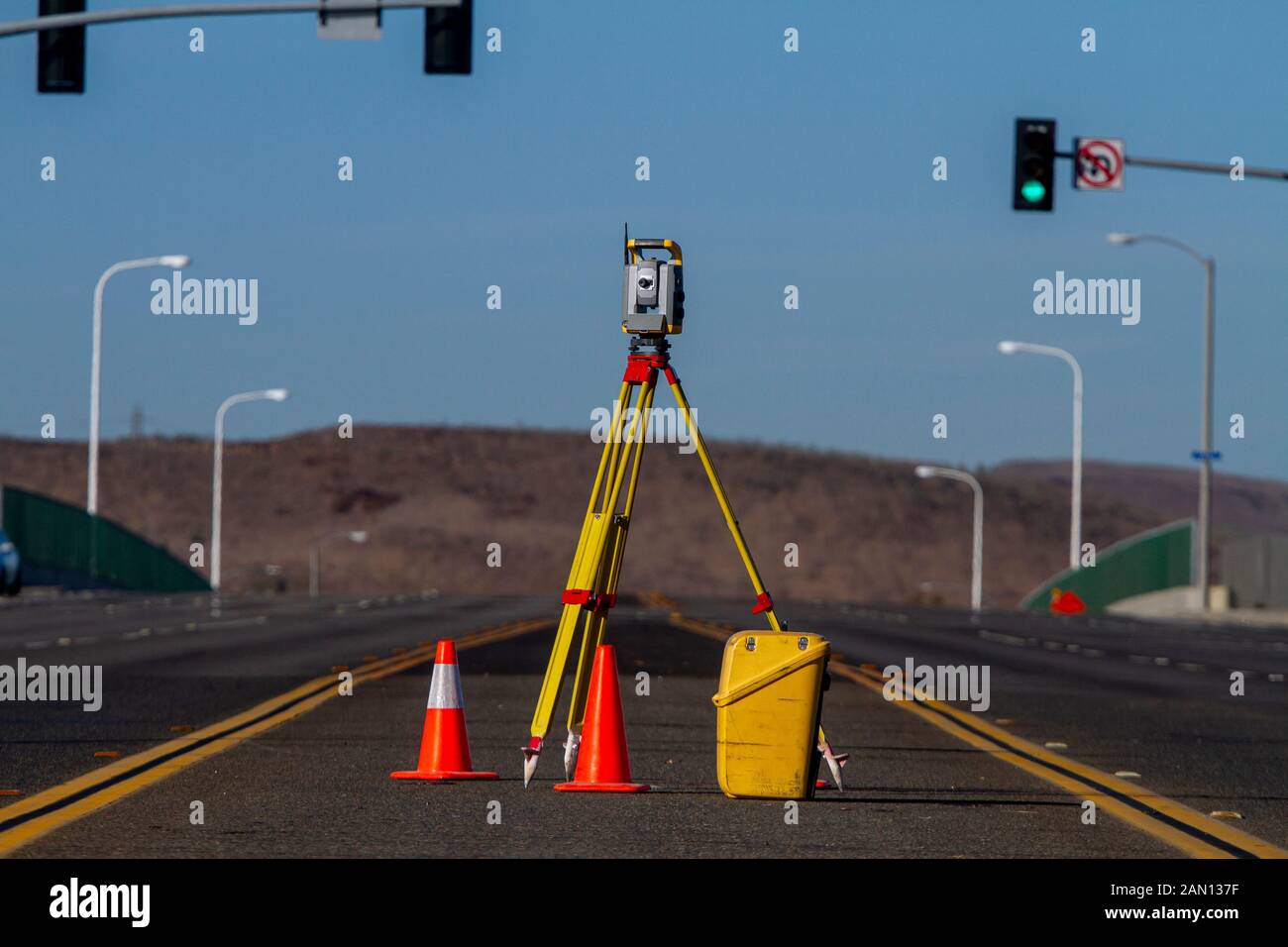 Land survey equipment set up on road with road becoming a hill in the background with traffic Stock Photo