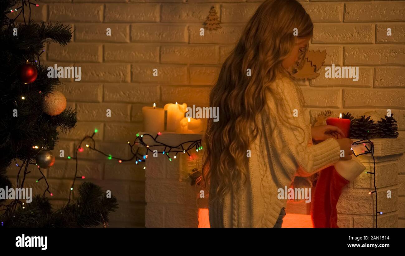 Long-haired blond girl hanging sock on fireplace waiting Santa Christmas miracle Stock Photo
