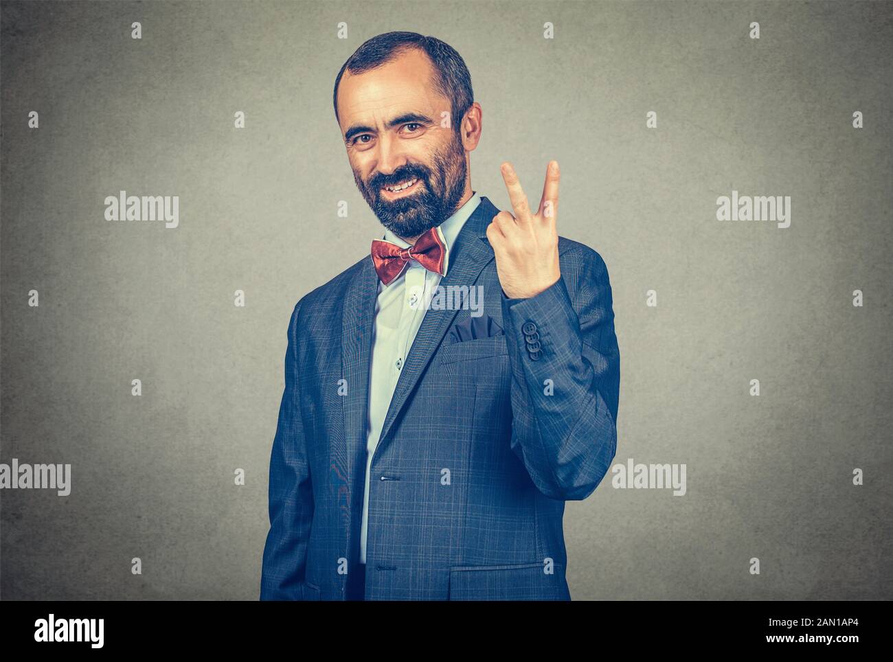 Portrait headshot middle aged businessman smiling with victory hand sign symbol isolated grey wall office background. Positive emotion face expression Stock Photo