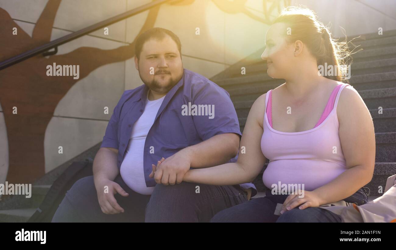 Obese man tenderly holding his fat girlfriend hand, true feelings, dating Stock Photo